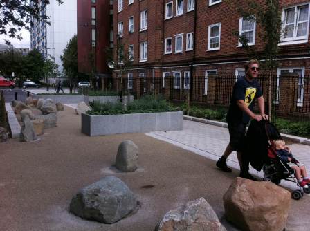 Man pushing child in pram through street blocked by boulders